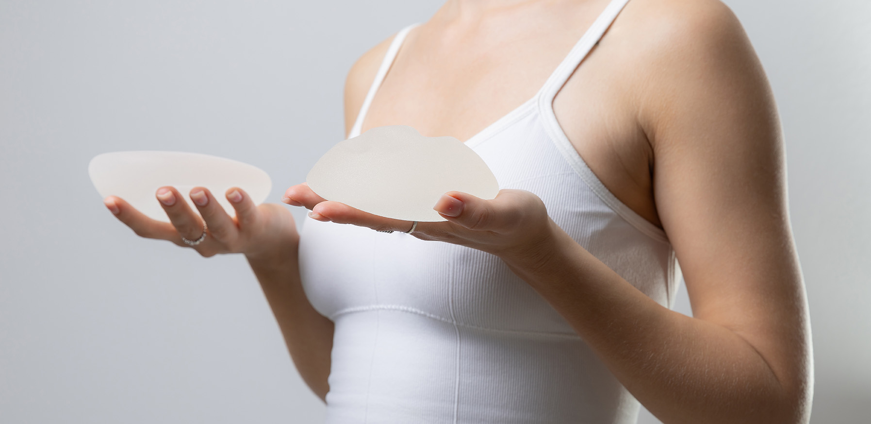 Woman holding silicone breast implants during preparation for breast augmentation.
