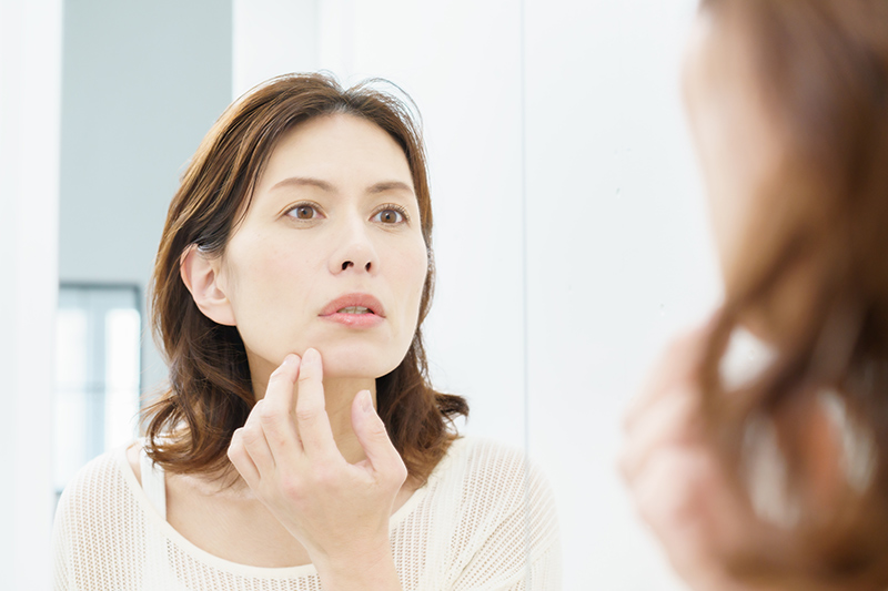 Woman looking in the mirror and noticing signs of facial ageing